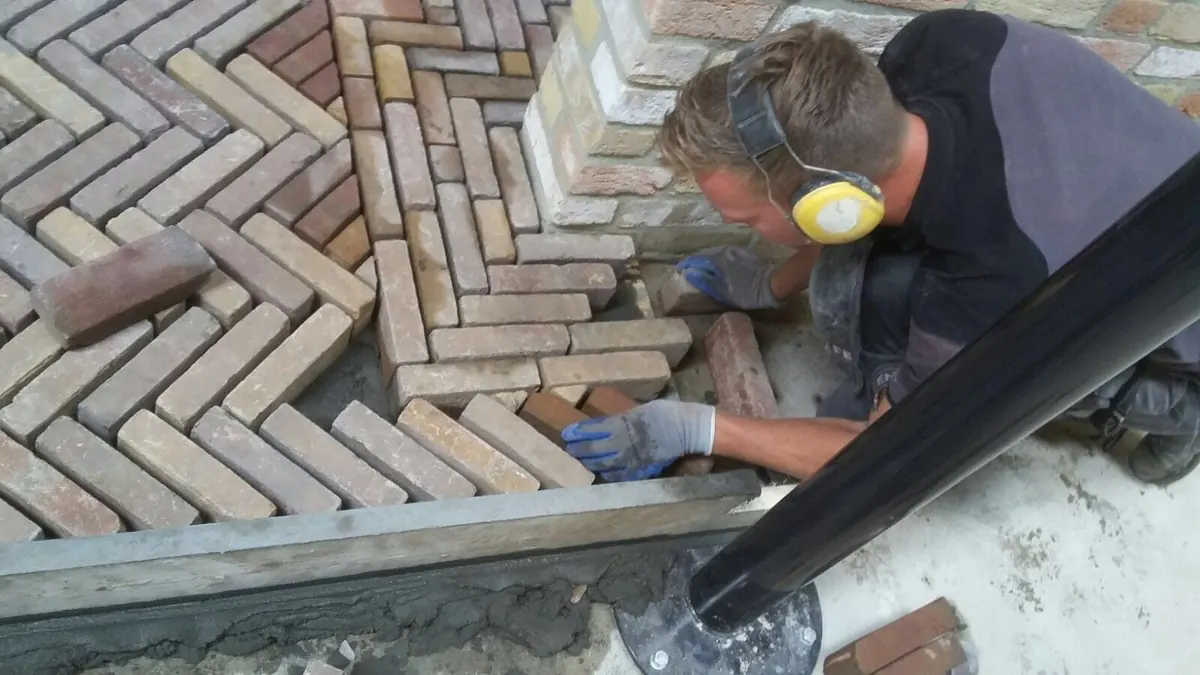 Hovenier legt oude gebakken klinkers in visgraatverband rond een gemetselde pilaar
